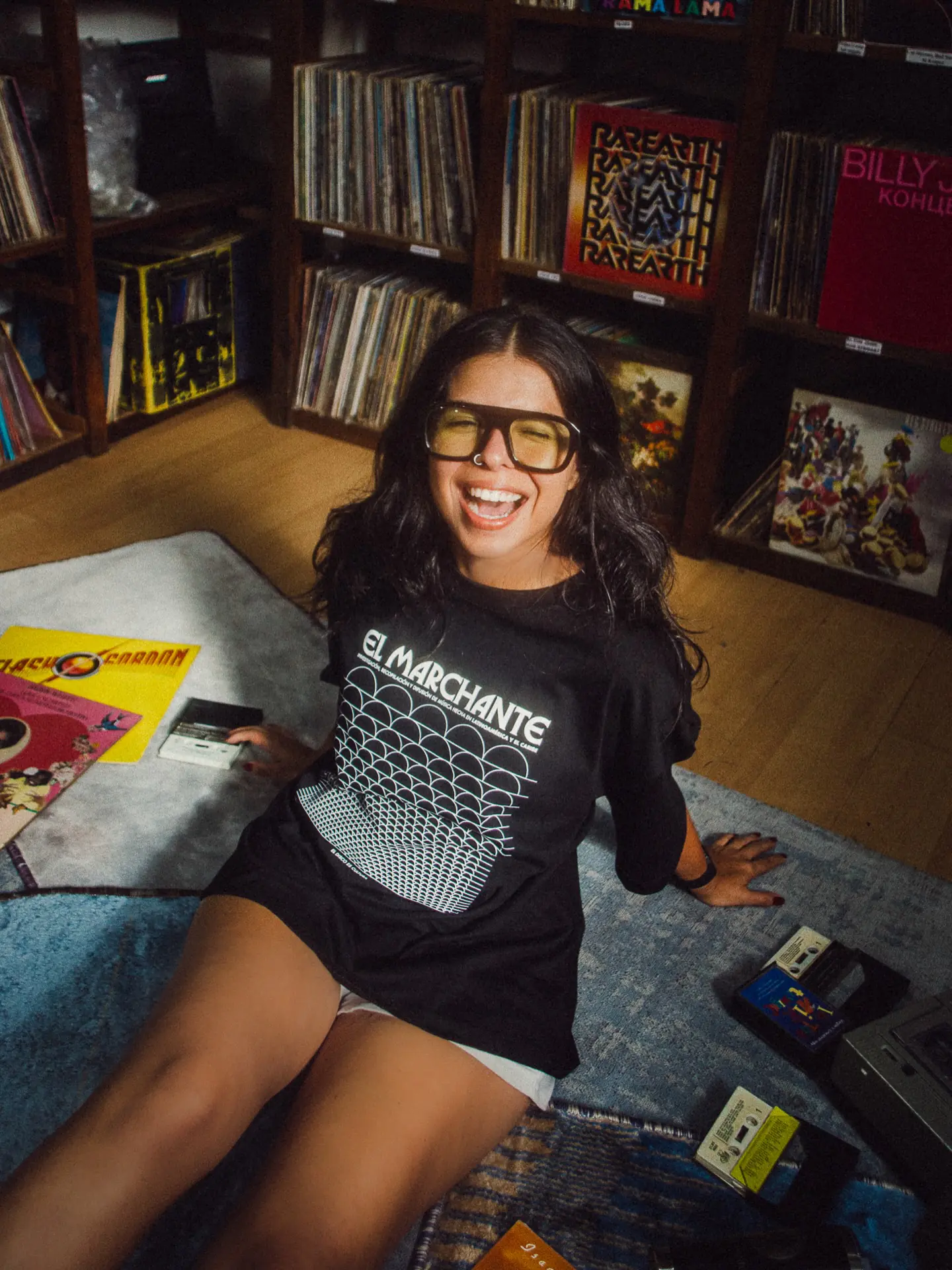 El Marchante T-Shirt by CRINI, worn seated with records