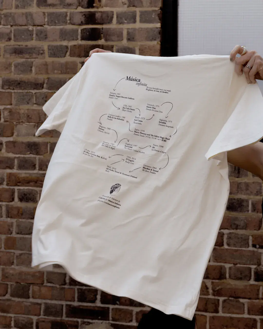 Música Infinita T-Shirt by CRINI, back print against a brick wall